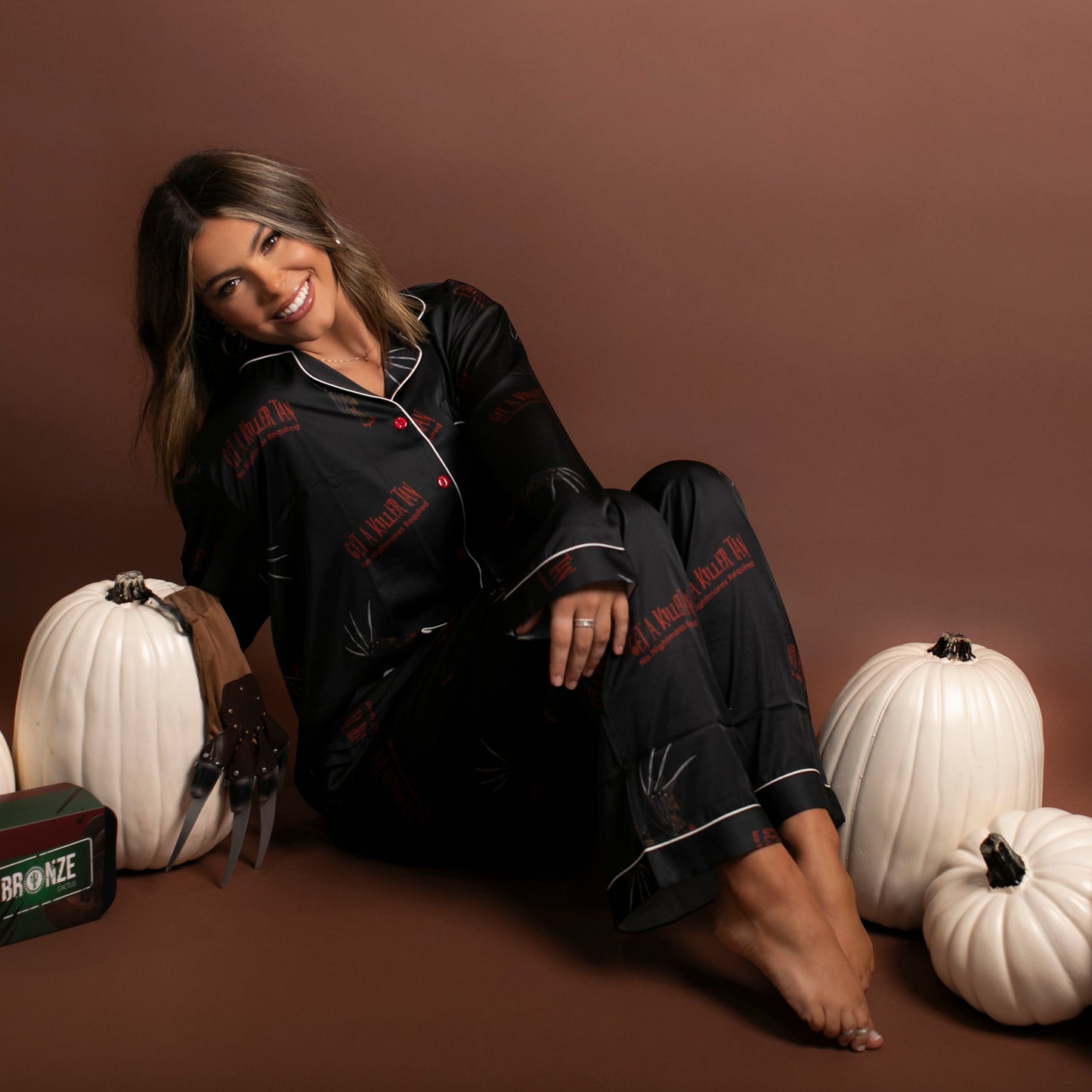 Woman in black pajamas sitting among white pumpkins and a hat on a brown background