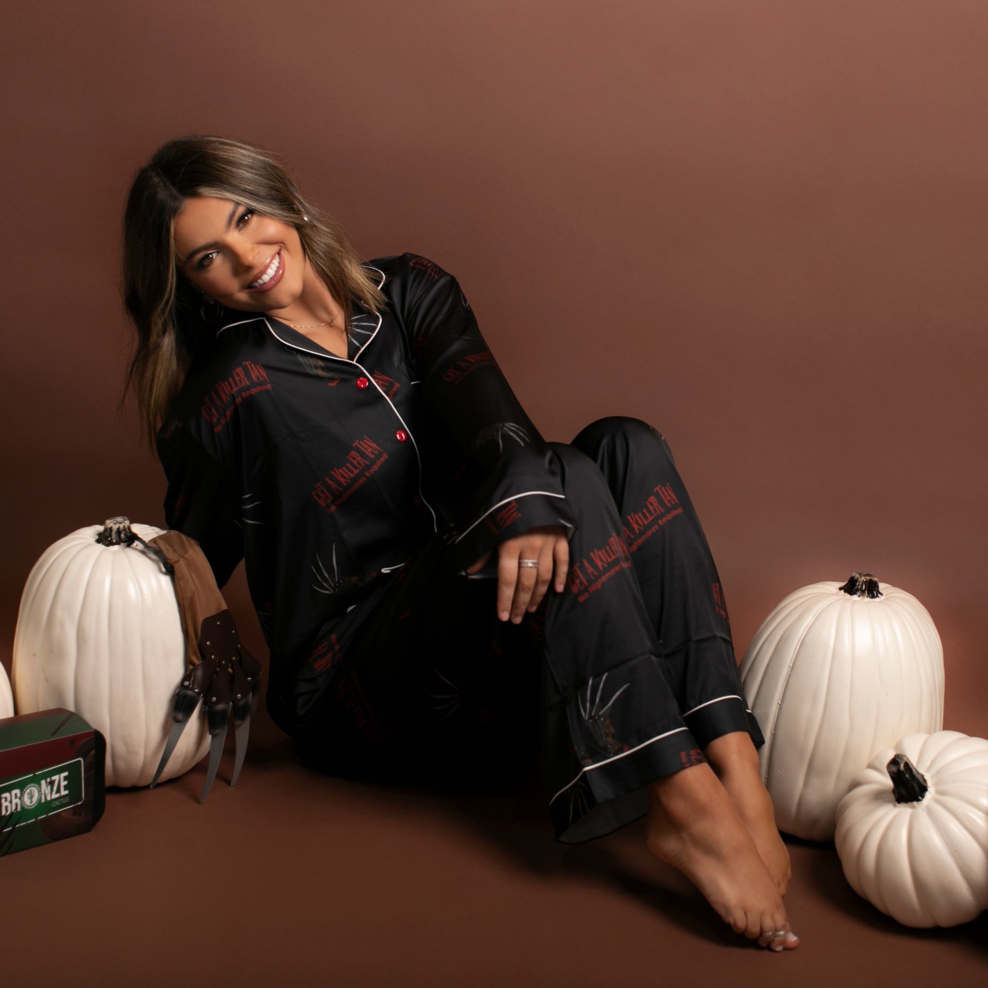 Woman in black pajamas sitting among white pumpkins and a hat on a brown background