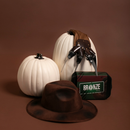 Three pumpkins with black and white designs, a brown hat, and a bag labeled 'Bronze' on a brown background.